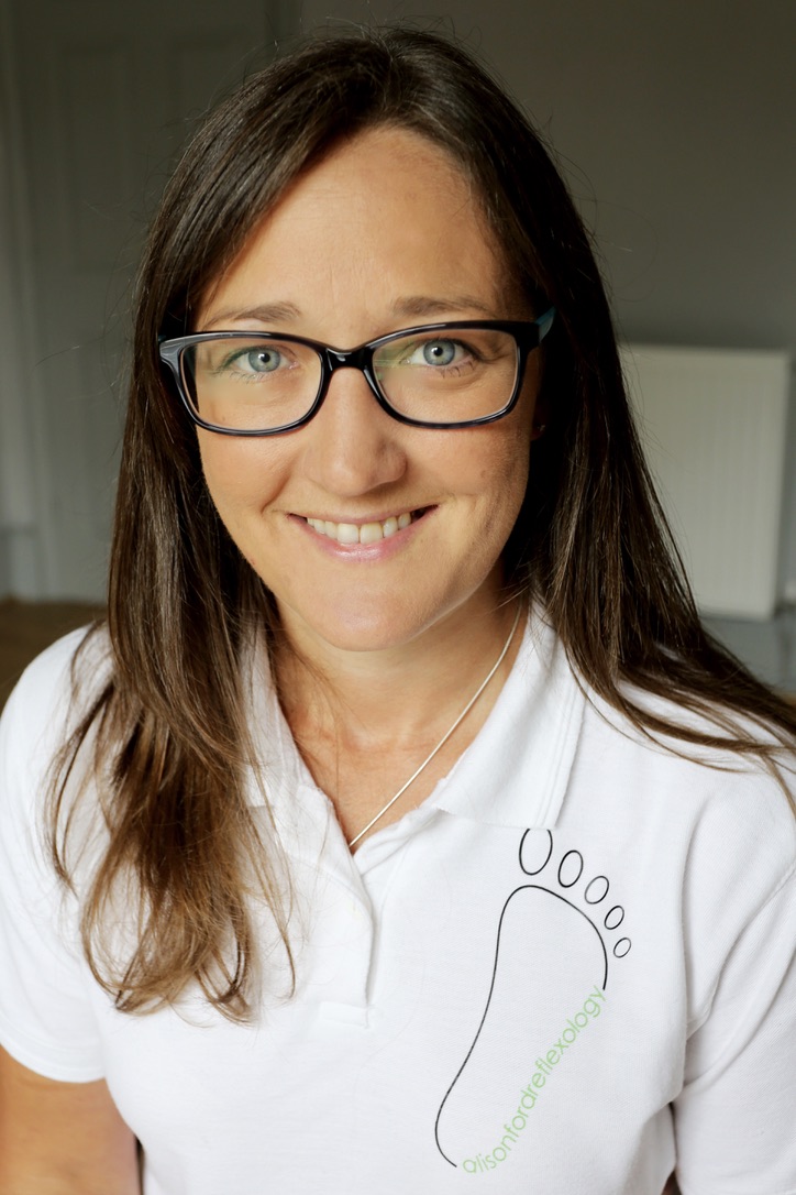 Ali Knight, a white woman with dark shoulder-length hair and glasses, smiling directly at the camera wearing a white reflexology branded polo shirt.